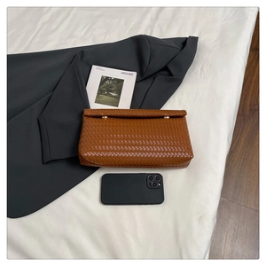 Dettaglio pochette in pelle intrecciata marrone con chiusura dorata e telefono per scala