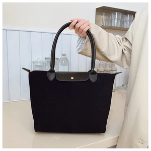 Detail of black tote bag with leather flap and gold snap button on beige coat background