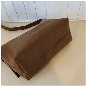 Detail of a brown leather shoulder bag showing the wide strap and folding base construction