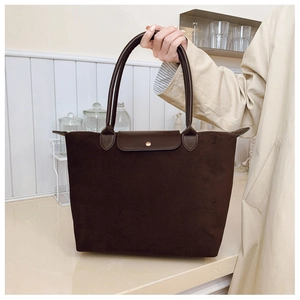 Close-up of brown suede tote bag featuring a leather flap and gold metallic snap button