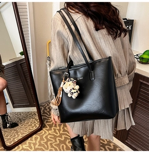 Close-up of black PU leather tote bag with a leopard plush kitty charm on the shoulder strap