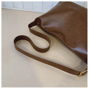 Close-up of brown textured leather bag with gold metal buckle and adjustable strap detail
