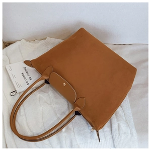 Close-up of tan suede tote bag with leather handles on a white knit sweater