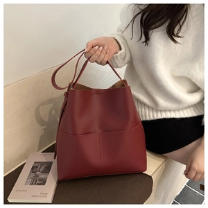 Detail of a deep red large bucket bag with leather texture and front pocket design