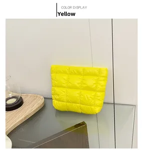 Detail view of yellow quilted puffer clutch bag with shiny textured fabric on glass surface