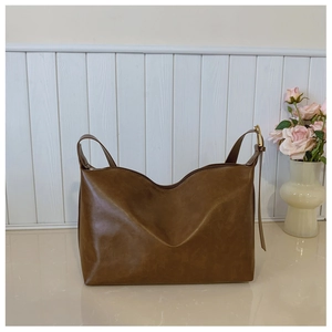 Detail of a brown tote bag featuring golden hardware and retro leather texture