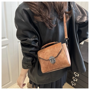 Detail view of a vintage brown leather bag with metallic clasp worn by a model