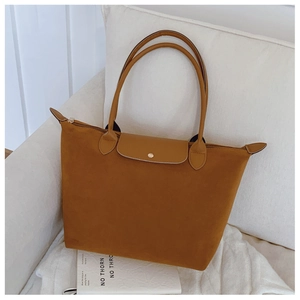 Close-up of caramel suede tote bag with metal buckle and leather handles on white sofa