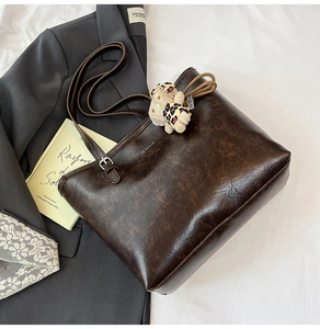 Detail of dark brown leather tote bag with leather texture and bear plush pendant charm