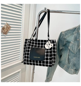 Detail of checkered tote bag with leather pocket, branding text and cute tiger charm