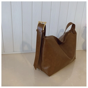 Detailed view of dark brown leather tote with a large gold buckle and wide shoulder strap