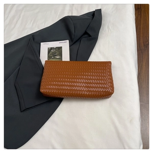 Dettaglio della trama in pelle intrecciata marrone su una pochette busta minimalista