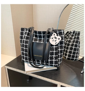 Detail of black and white tweed tote bag with leather pocket and cat charm on white books