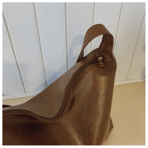 Detail of dark brown leather handbag featuring gold zipper and wide shoulder strap