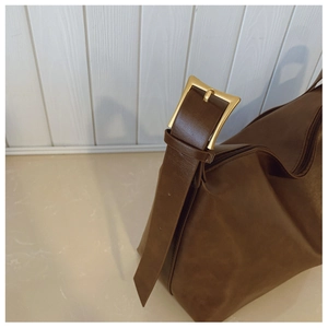 Detail of dark brown leather tote showing gold metal buckle and smooth matte texture