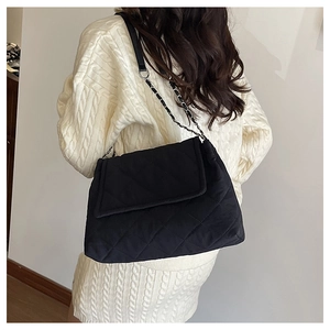 Detailed view of black quilted chain strap bag worn with white knit sweater