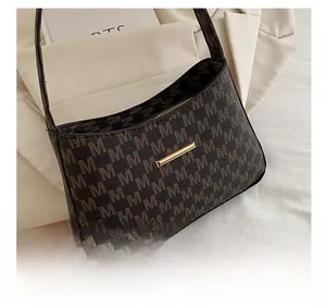 Close-up of deep brown monogram underarm bag with golden metal bar and M pattern