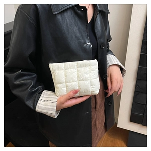 Close-up of a cream quilted padded clutch bag held by a person in a leather jacket