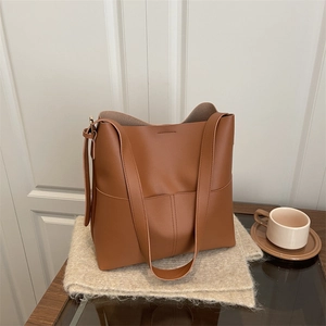Caramel brown leather hobo bucket bag with front pocket on a beige knit scarf