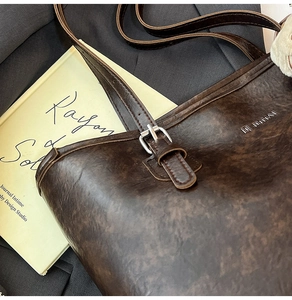 Detail of vintage dark brown leather tote bag with metallic logo and textured finish