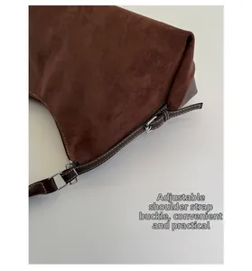 Detail of adjustable silver buckle and white stitching on brown suede shoulder bag strap