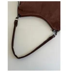Detail view of dark brown suede shoulder bag with white contrast stitching and silver zipper