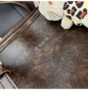 Close-up of deep brown leather tote bag texture with metal logo and leopard cat charm