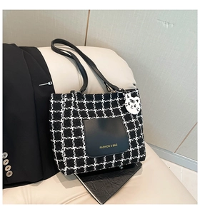 Detail of tweed tote bag with black leather pocket and a white cat charm accessory