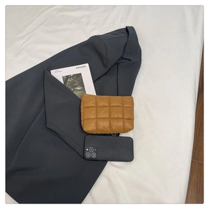 Close-up of camel quilted pouch with grid stitching on a grey suit jacket and magazine