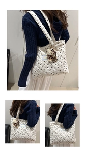 Close-up of white quilted tote bag featuring black heart prints and blue woven label detail