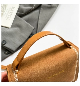 Détail du sac en daim marron avec ferrures dorées et surpiqûres blanches tressées