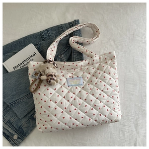 Close-up of white quilted tote bag with red hearts and plush bear charm on white fabric