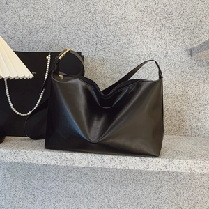 Minimalist black large capacity shoulder bag with gold hardware on gray stone steps