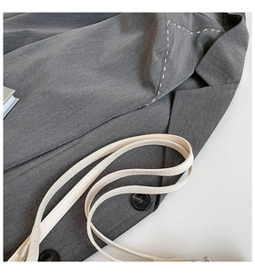 Detail shot of grey blazer lapel with white stitching and textured black button