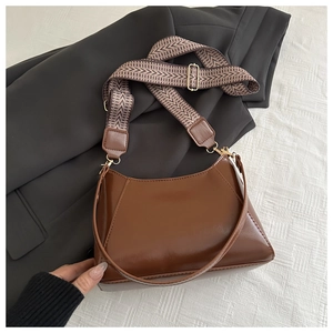 Detail der tiefbraunen glänzenden Ledertasche mit gemustertem breitem Web-Schultergurt