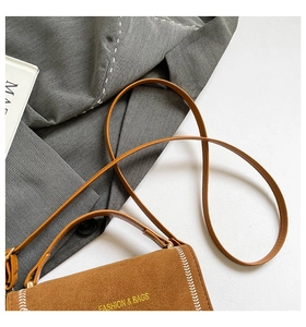 Détail du sac bandoulière en daim marron avec surpiqûres blanches et logo doré devant
