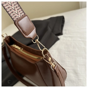 Close-up of brown faux leather shoulder bag with gold zipper and woven pattern strap