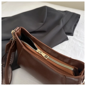 Detail of a brown leather bag showing golden metal zipper and houndstooth shoulder strap