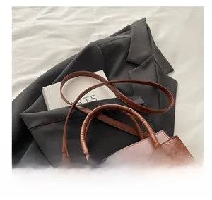Detail of brown crocodile pattern square bag with dual straps on grey suit background