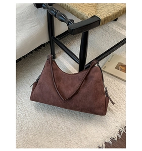 Détail d'un sac à bandoulière en daim givré marron foncé posé contre une chaise en bois