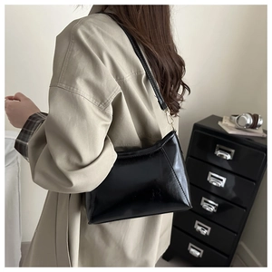 Glossy black underarm shoulder bag with gold metal buckle detail shown with trench coat