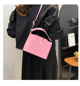 Pink bucket bag with gold V-shaped buckle worn with a casual black outfit for women