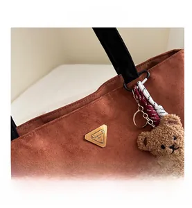 Détail du cabas en daim marron avec plaque logo métallique et breloque ours en peluche