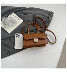 Detailed view of brown quilted handbag with gold hardware on dark suit fabric