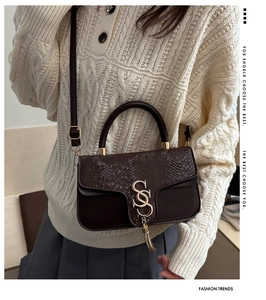 Detailed view of snake-embossed leather handbag with gold SS buckle and elegant tassel