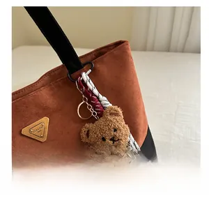 Détail d'un charm ours en peluche avec cordon tressé et clip doré sur sac en daim