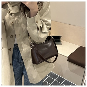 Detail of dark brown tote bag with gold studs and metallic buckles on beige coat