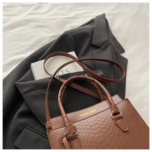 Detail of brown crocodile pattern PU leather handbag with gold hardware and logo