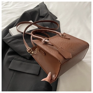 Detail of brown crocodile pattern leather handbag with handle on black blazer background