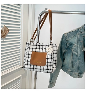 Detail of checkered tote bag with brown leather pocket and a white cat-shaped charm